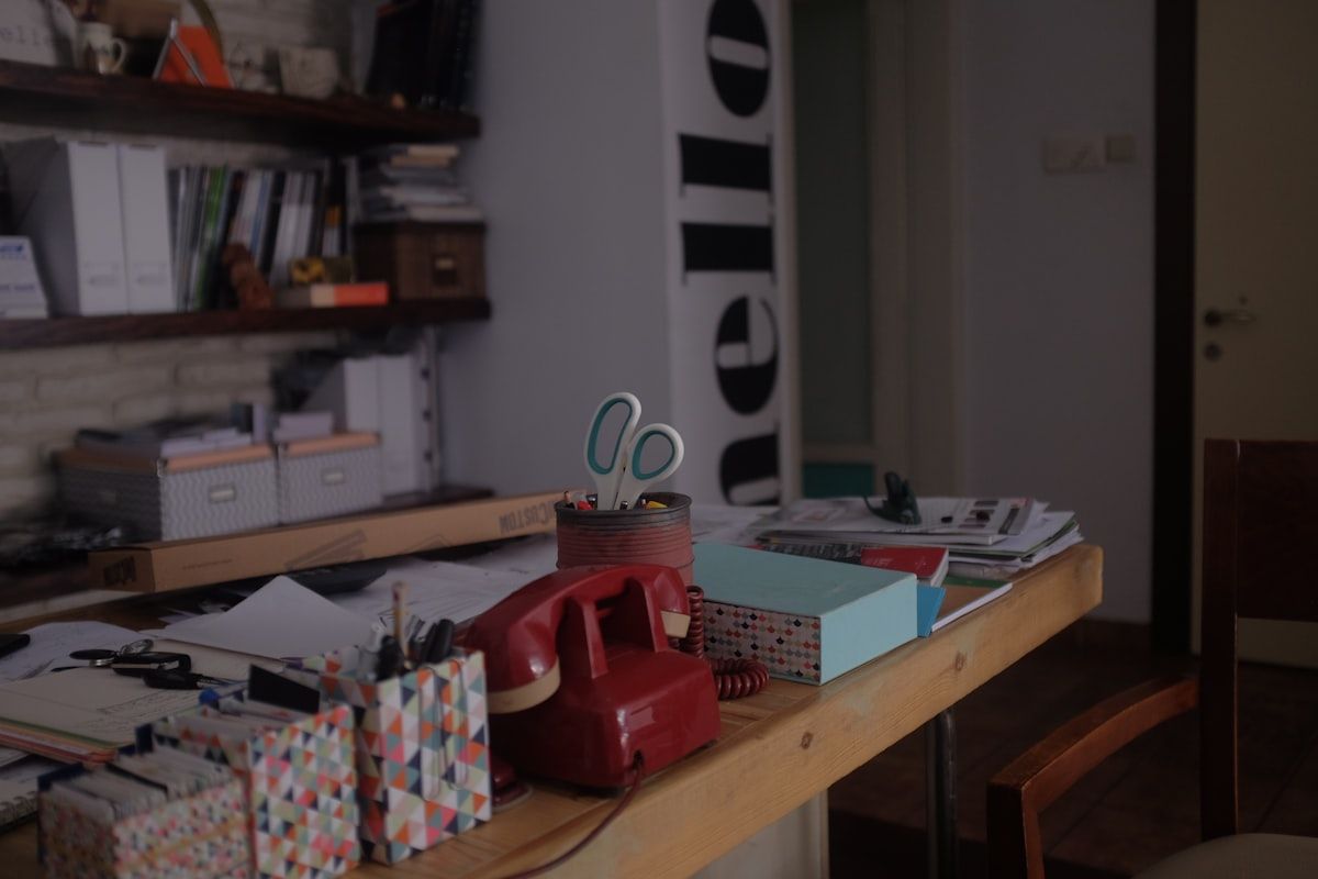 A kitchen table covered with a moving planner, calendar pages, sticky notes, and grouped packing supplies, with boxes and folded clothes arranged by week as if the move is being scheduled step by step