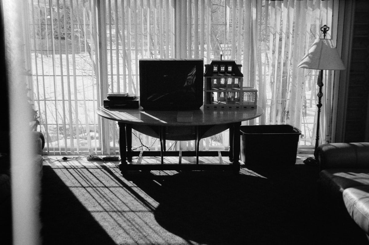 Three moving company estimates spread across a table beside a clipboard, a magnifying glass, and a calculator, with a moving truck parked outside a house in the background