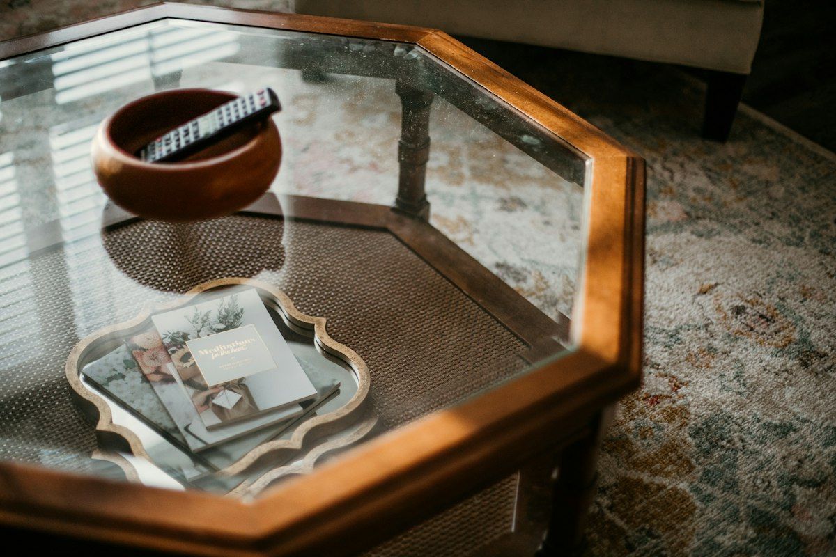 An organized home moving scene with open boxes grouped by room, a crew carefully wrapping a glass tabletop and a framed mirror in protective padding, labeled boxes stacked by the front door, and a partially packed living room with furniture being prepared for loading.
