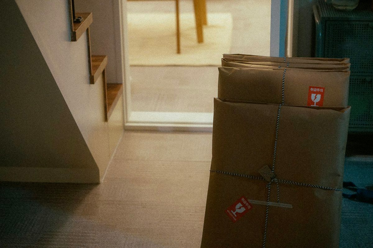 A packed living room with moving supplies spread out around furniture, showing small and large boxes, rolls of tape, bundles of packing paper, and a few specialty cartons for fragile items, with one area set up for a long-distance move and another for a smaller local move