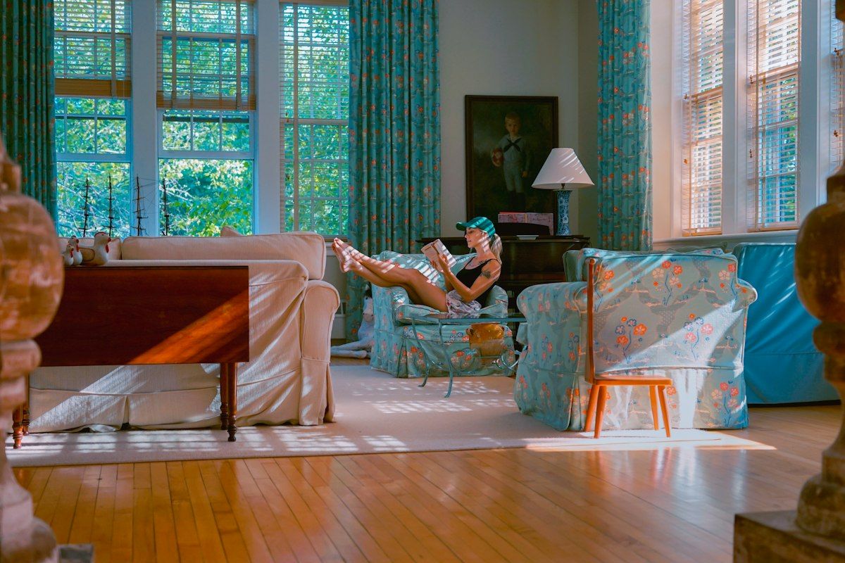 A moving crew packing a living room into labeled boxes, with wrapped picture frames leaning against a wall, a padded sofa ready for loading, a dish pack open on the floor, and piles of packing paper and tape showing the room-by-room workflow.