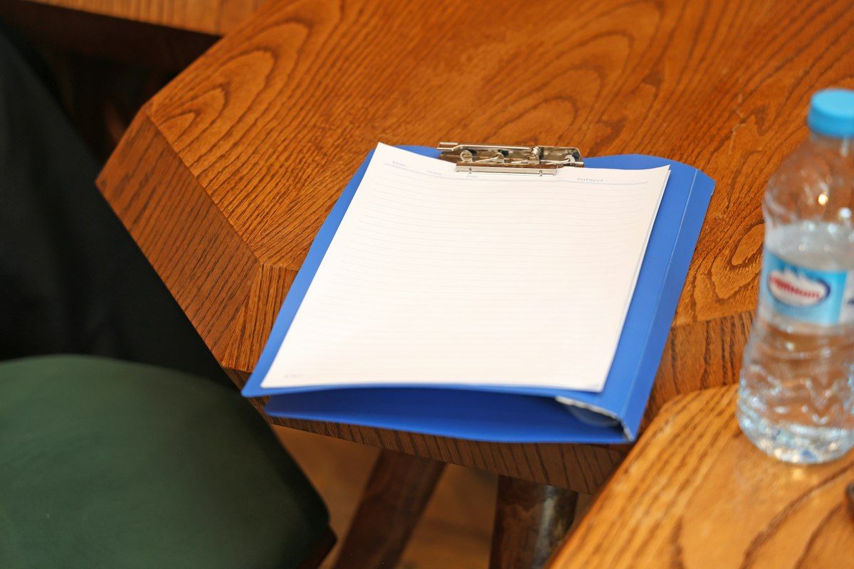 A clipboard beside a packing table showing a detailed moving estimate packet with separate pages for hourly labor, distance, stair carry, furniture wrapping, and specialty-item charges, next to a hand truck, moving blankets, and a partially disassembled sectional sofa